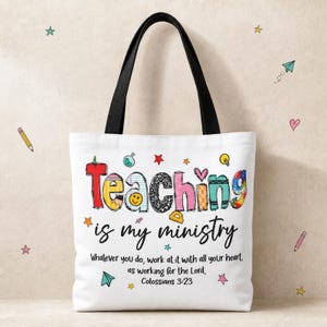 Op de afbeelding: Een witte draagtas met zwarte hengsels voorzien van de kleurrijke tekst Teaching is my ministry in een speels lettertype. Daaronder staat de tekst Whatever you do, work at it with all your heart, as working for the Lord, Colossians 3:23. Kleine sterretjes en hartjes versieren de tas.