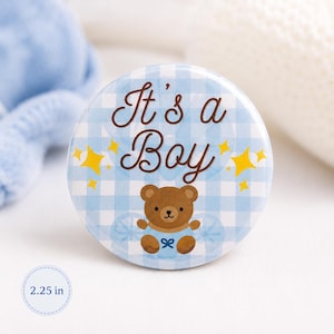 May include: A circular pinback button measuring 2.25 inches in diameter, featuring a light blue and white gingham pattern, the brown text It's a Boy, yellow star accents, and a central illustration of a brown teddy bear wearing a blue bow.
