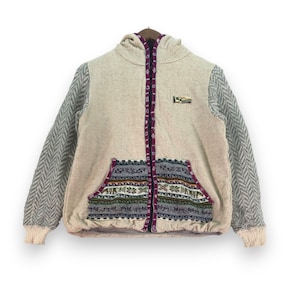 May include: A cream-coloured hooded jacket with a zip fastening and a patterned pocket. The jacket has a herringbone pattern on the sleeves and a woven patch on the front that says "The Mountain".