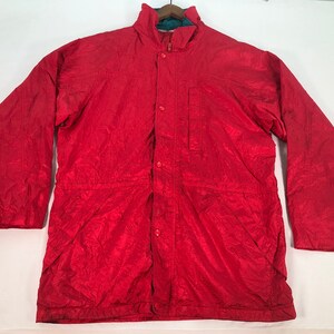 May include: A red, lightweight jacket with a zipper and button closure. The jacket has a stand-up collar and a single pocket on the left chest.