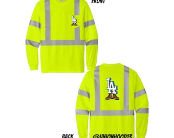 May include: A bright yellow long-sleeved shirt with reflective silver stripes. The shirt has a graphic of the LA Dodgers logo on the front and back. The back of the shirt also has the text "@UNIONHOOD13".