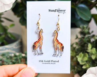 May include: A pair of gold plated giraffe earrings with clear crystal beads. The earrings are on a white card with the text "Sunflower Strange" and "18K Gold Plated Created by Kayli."