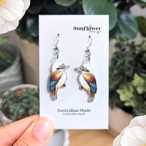 K&ouml;nnte beinhalten: Ein Paar silberne Ohrringe mit einem farbenfrohen Kookaburra-Design. Die Ohrringe befinden sich auf einer wei&szlig;en Karte mit dem Text "Sunflower Strange" und "Australian Made, Created by Kayli."