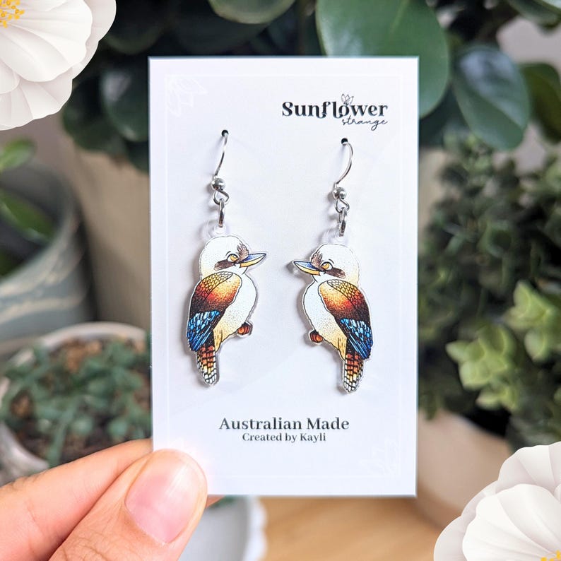 K&ouml;nnte beinhalten: Ein Paar silberne Ohrringe mit einem farbenfrohen Kookaburra-Design. Die Ohrringe befinden sich auf einer wei&szlig;en Karte mit dem Text "Sunflower Strange" und "Australian Made, Created by Kayli."