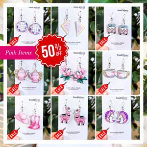 May include: A selection of pink earrings featuring diverse designs such as disco balls, toast, camper vans, teapots, lotus flowers, teacups, a cowboy hat and boots, llamas, and unicorns. Each pair has a silver hook. The image includes a "50% OFF" sale banner.