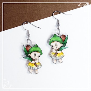 May include: A pair of earrings featuring a whimsical illustration of a fairy-like figure with a green hat, holding a yellow flower and a brown stick. The earrings are made of clear acrylic and have silver hooks.