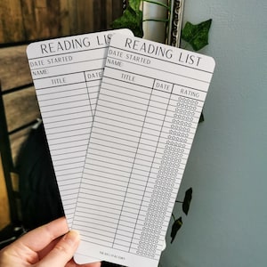May include: Two white reading list cards with black text and lines. The cards have sections for the book title, date started, date finished, and a rating system with five stars.