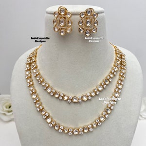 Peut inclure: Un collier en or avec deux rangs de pierres blanches. Le collier est assorti à des boucles d'oreilles. Les boucles d'oreilles sont également en or avec des pierres blanches. Le collier et les boucles d'oreilles sont étiquetés "IndoExquisite Designs".
