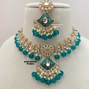 May include: A gold necklace and earrings set with a green enamel design and white pearl accents. The necklace features a large pendant with a green enamel design and white pearl accents. The earrings are a matching design with a smaller pendant.
