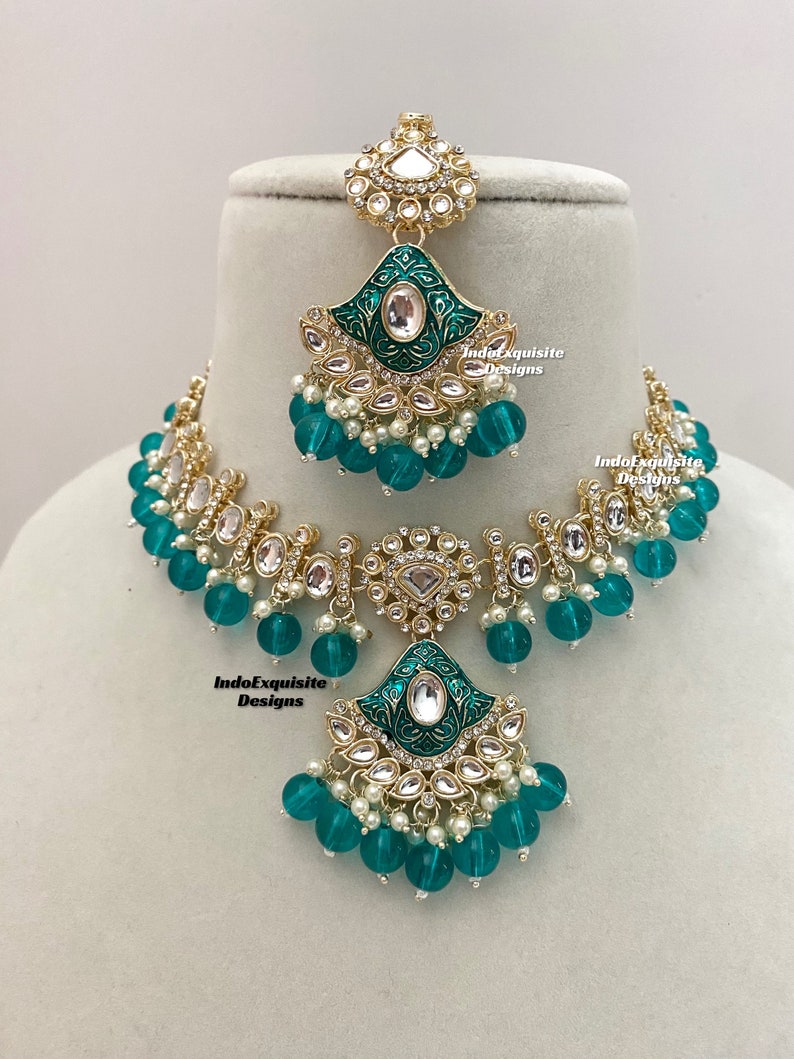 May include: A gold necklace and earrings set with a green enamel design and white pearl accents. The necklace features a large pendant with a green enamel design and white pearl accents. The earrings are a matching design with a smaller pendant.