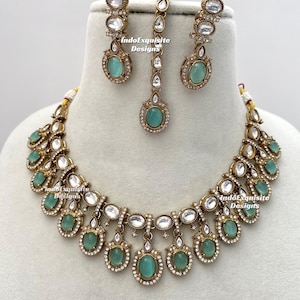 Puede incluir: Un conjunto de joyas dorado que incluye un collar, pendientes y una pieza para la cabeza. El conjunto presenta gemas ovaladas de color verde claro y detalles claros y brillantes. El collar y los pendientes tienen un diseño a juego.