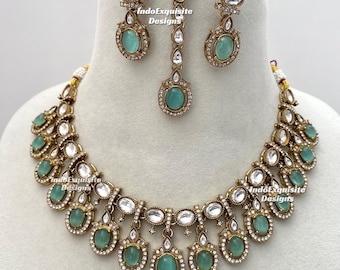 May include: A gold-toned jewelry set featuring a necklace, earrings, and a headpiece. The set includes oval, light-green gemstones and clear, sparkling accents. The necklace and earrings have a matching design, and the headpiece has a central gemstone.