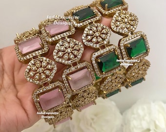 Puede incluir: Un conjunto de brazaletes dorados con piedras rectangulares rosas y verdes alternas, intercaladas con motivos florales circulares incrustados con pequeños cristales transparentes. Las superficies metálicas son texturizadas y el texto IndoExquisite Designs es visible.