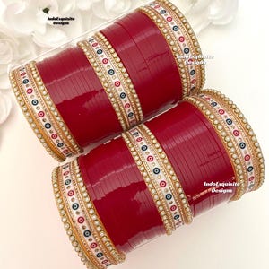 Può includere: Un set di braccialetti rossi con accenti decorativi bianchi e dorati. I braccialetti sono adornati con piccole perle bianche e disegni colorati. Il testo "IndoExquisite Designs" è visibile sui braccialetti.