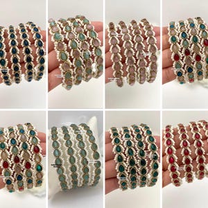 Peut inclure: Une collection de huit ensembles de bracelets joncs ornés de pierres en forme de goutte d'eau dans des tons variés de bleu, rose, rouge et vert. Chaque bracelet est agrémenté de petites perles blanches sur les bords, offrant un aspect texturé.