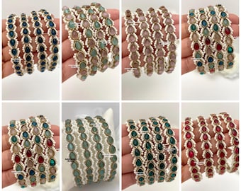 May include: A collection of eight sets of bangles featuring teardrop-shaped stones in various colors, including blue, pink, red, and green. Each bangle is accented with small white beads along the edges, creating a decorative, textured appearance.