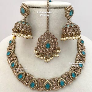 May include: An antique-style jewelry set featuring a necklace, earrings, and a headpiece. The set has a bronze finish with teal-colored teardrop-shaped stones and small white pearls. The earrings are bell-shaped. The text "IndoExquisite Designs" is visible.