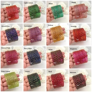 May include: A collection of sixteen sets of bangles, each featuring a stack of thin, translucent glass bracelets in various colors including coral pink, light green, mint, pink, royal blue, lavender, yellow, orange, onion pink, navy blue, wine, magenta, lime green, green, red, and maroon, all accented with small gold glitter particles.