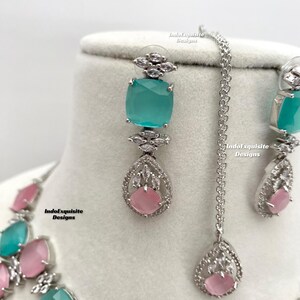 May include: A silver necklace and earrings set with a teardrop pendant and square stones. The stones are a mix of light pink and turquoise.