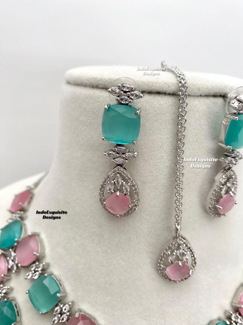 May include: A silver necklace and earrings set with a teardrop pendant and square stones. The stones are a mix of light pink and turquoise.