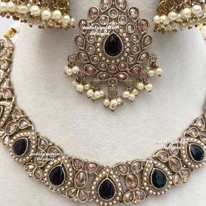 May include: An ornate jewelry set featuring a necklace, earrings, and a headpiece. The set is gold-toned with black teardrop-shaped stones and small white pearls. The necklace and headpiece have a floral design.