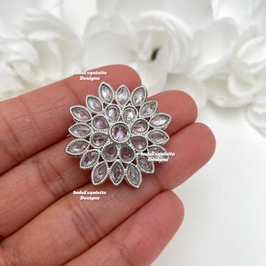 May include: A silver ring with a large, clear, flower-shaped design. The ring is set with many small, clear stones.