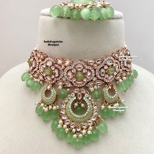 May include: A green and gold choker necklace with a large, ornate pendant. The pendant is decorated with pearls, rhinestones, and a green enamel design. The necklace is accented with green beads.