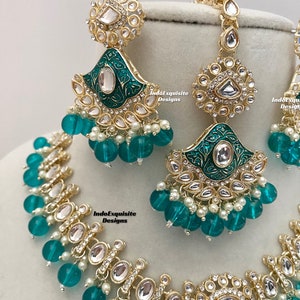 May include: A gold and green Indian bridal necklace set with teardrop-shaped pendants, clear stones, and green glass beads. The set includes a necklace, earrings, and a maang tikka.