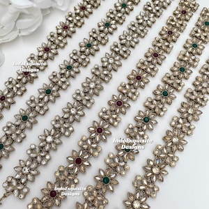 Może przedstawiać: Pięć złotych łańcuszków do włosów z przezroczystymi, czerwonymi i zielonymi kamieniami. Łańcuszki są wykonane z małych ogniw w kształcie kwiatów.