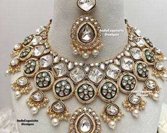 May include: A gold and white necklace set with green accents. The necklace features a large, round pendant with a clear stone in the center. The set also includes a matching earring.