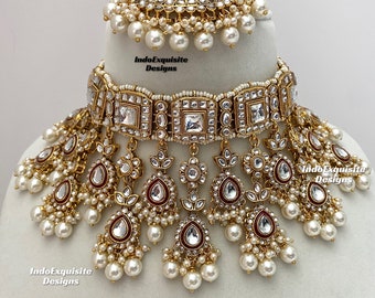 May include: A gold and white bridal necklace set with a large, ornate pendant and multiple strands of pearls. The set includes a matching maang tikka.