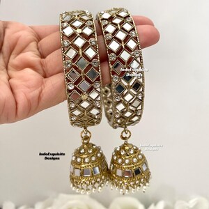 May include: A pair of gold-tone bangles with mirrored squares and clear rhinestones. The bangles are attached to gold-tone jhumka earrings with mirrored squares and white pearls.
