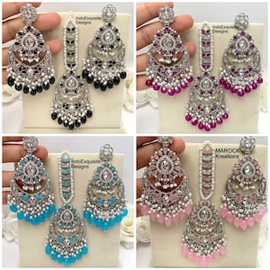 May include: Four sets of silver earrings and maang tikka, a traditional Indian headpiece. The earrings feature a crescent moon design with colorful stones and pearls. The maang tikkas are a chain with a pendant. The colors are black, pink, blue, and turquoise.