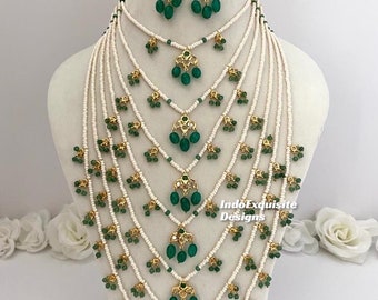 May include: A multi-strand necklace with green and gold accents. The necklace is made of white beads and features a cascading design of green stones. The necklace is paired with matching earrings.
