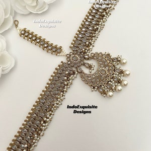 May include: Gold and white bridal headpiece with a large, ornate, crescent-shaped design and a smaller, matching piece that attaches to the hair. The headpiece is decorated with clear rhinestones and pearls.