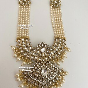 May include: An ornate necklace featuring multiple strands of faux pearls. The necklace has gold-toned metal accents with clear, sparkling stones and dangling pearl drops. The design includes floral and geometric shapes, creating an elegant and detailed piece of jewelry.