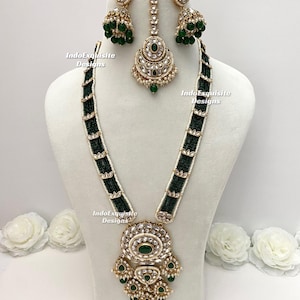 May include: A gold-toned jewellery set comprising a necklace, earrings, and a headpiece. The necklace features a large pendant with green gemstones and black beaded sections. The earrings and headpiece echo the pendant's design, with green beads and gold detailing.