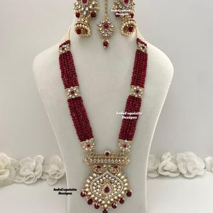 May include: A maroon and gold necklace set with a large pendant featuring intricate detailing and red and white stones. The set also includes matching earrings with a similar design.