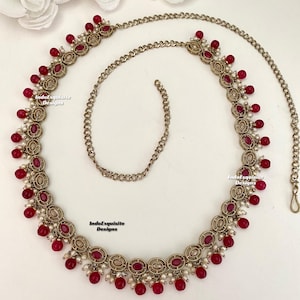 May include: A gold chain belt with red and white beads. The chain is made of small, linked circles. The beads are oval-shaped and have a shiny finish. The belt is decorated with small, white stones.