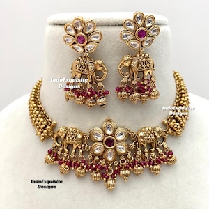 Peut inclure: Un collier en or avec un pendentif floral et trois breloques en forme d'éléphant. Le collier est orné de perles rouges et est accompagné d'une paire de boucles d'oreilles assorties avec un motif floral et des breloques en forme d'éléphant.