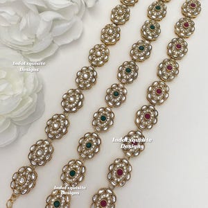 Może przedstawiać: Trzy złote łańcuszki z owalnymi ogniwami, każde ogniwo ozdobione jest białymi cyrkoniami i jednym kolorowym kamieniem szlachetnym. Kamienie szlachetne są zielone, czerwone i zielone.