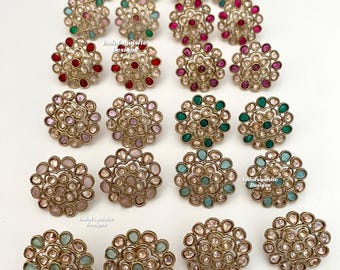 Puede incluir: Una colección de pendientes circulares dispuestos en filas, con monturas de metal dorado y piedras en forma de lágrima de varios colores, incluyendo rojo, rosa, verde, azul y transparente. El texto IndoExquisite Designs es visible.