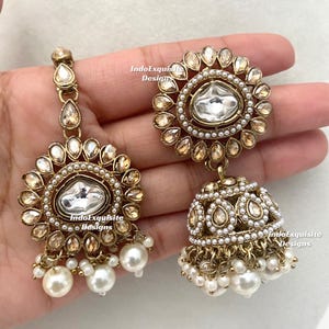 May include: Gold-toned earrings with a floral design, featuring clear and champagne-colored stones, and white pearl accents. The earrings have a dangling bell shape with multiple pearl drops.