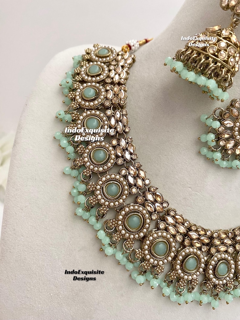 May include: A gold and silver necklace with light blue stones and pearl accents. The necklace is part of a set that includes matching earrings.
