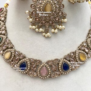 May include: An ornate, antique-style jewelry set featuring a necklace, earrings, and a headpiece. The set is silver-toned with a variety of colorful gemstones, including blue, pink, and yellow, and is accented with small pearls. The headpiece has a central teardrop-shaped stone.