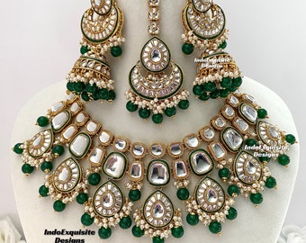 May include: A gold and green Indian bridal necklace set with a large, ornate pendant and matching earrings. The necklace features a layered design with multiple tiers of round and rectangular stones, accented with green beads. The earrings are similarly designed with a teardrop shape and green beads.