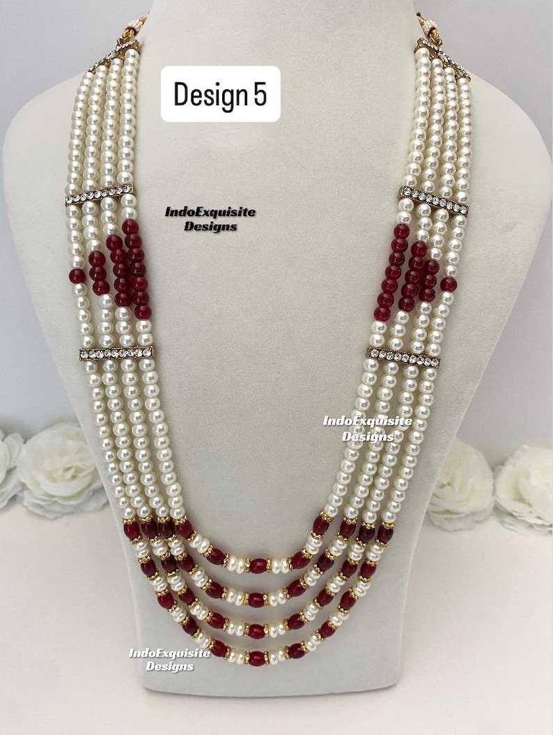 May include: A multi-strand necklace with white faux pearls and burgundy beads. The necklace has gold-colored accents and rhinestone-studded bars. The text "Design 5" and "IndoExquisite Designs" are visible.