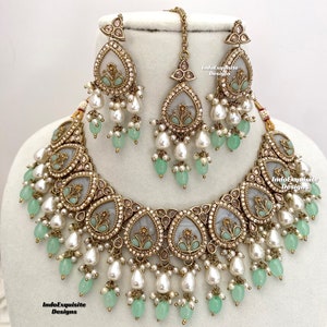 Könnte beinhalten: Antikes goldfarbenes Schmuckset mit Halskette, Ohrringen und Haarschmuck. Der Schmuck hat tropfenförmige Anhänger mit hellblauem Mittelteil, verziert mit Perlen und mintgrünen Perlen. Das Set ist mit kleinen Kristallen und floralen Details verziert.