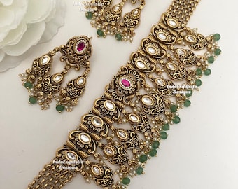 Puede incluir: Un conjunto de collar y pendientes en tono dorado con intrincado trabajo en metal, piedras blancas ovaladas, piedras rosas centrales y cuentas verdes colgantes con pequeñas perlas blancas. El collar tiene un diseño de cadena ancha.