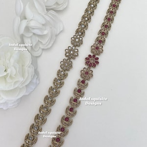 Może przedstawiać: Dwa złote łańcuszki z naprzemiennymi wzorami półksiężyca i kwiatów. Łańcuszek po lewej stronie ma w kwiatach przezroczyste kamienie, podczas gdy łańcuszek po prawej stronie ma w kwiatach czerwone kamienie. Oba łańcuszki mają około 50 cm długości.